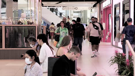 Tourists-and-shoppers-are-busy-window-shopping-for-designer-fashion-brands,-while-some-are-just-sitting-and-checking-their-mobile-phones-inside-a-mall-in-Bangkok,-Thailand