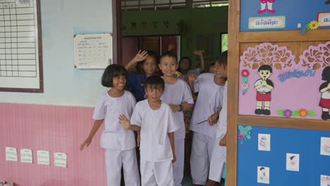 Thai-kids-bid-a-fond-farewell-with-waves,-their-smiles-echoing-the-warmth-of-shared-moments-and-goodbyes-at-the-doorway