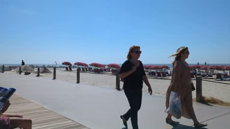 Coronado-beach-promenade-with-pedestrians,-sunbrellas-and-loungers-on-a-sandy-beach