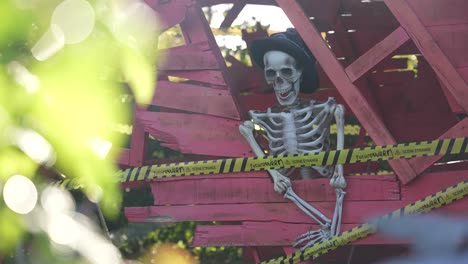 Skeleton-for-a-Halloween-display-at-Futuroscope-theme-park-behind-caution-tape-wearing-a-hat,-Long-handheld-shot
