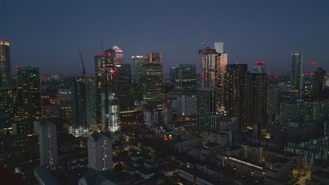 Drone-push-in-toward-illuminated-Canary-Wharf-skyline-at-twilight,-East-London