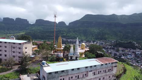 Vista-Aérea-Panorámica-Del-Templo-Sagrado-Nil-Parvat-En-Los-Bordes-De-Las-Colinas-Brahmagiri-Con-La-Vista-De-La-Ciudad-De-Trimbakeshwar-Al-Fondo,-Nashik,-Maharashtra,-India