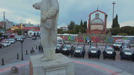 Vertical-pan-of-7-police-pick-ups-and-2-ambulances-with-armed-officers-of-the-Police-Department-lined-up-and-posing-in-front-of-their-cars-and-behind-a-statue-of-President-Benito-Juarez