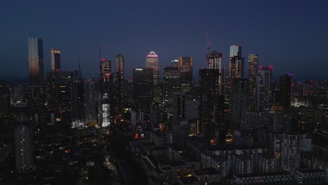 Filmische-Luftaufnahme-über-Die-Futuristischen-Wolkenkratzer-Der-Stadt-Canary-Wharf-In-London-Mit-Beleuchteten-Türmen