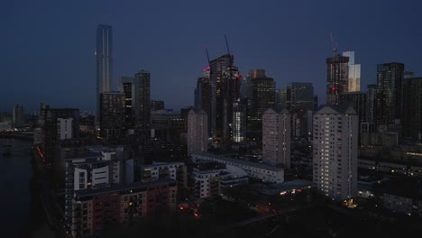 Aerial-view-circling-above-London-Canary-Wharf-high-rise-cityscape-skyscrapers-during-blue-hour
