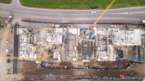 Aerial-top-down-shot-of-construction-site-with-cranes-and-driving-cars-on-road