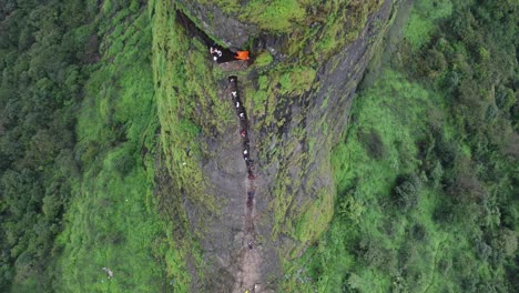 Drone-shot-of-ancient-Harihar-Fort-with-tourists-climbing-down-steep-and-vertical-stairs-during-monsoon-trek,-Harshewadi,-Nashik,-Maharashtra,-India