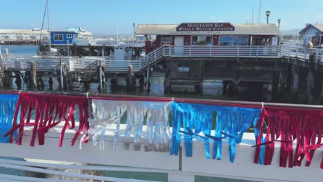 Colourful-flags-on-wooden-fence-on-the-pier-of-Monterey's-Fisherman's-Wharf-and-whale-watch-centre-with-ocean-bay-waters