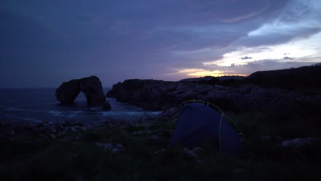 Remote-wild-camping-tent-near-unique-rock-formation-ocean-cliff-waves