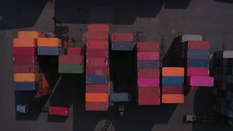 Shipping-containers-in-port-with-vehicles-in-strong-morning-light-from-top-down-aerial-shot
