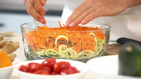 Massaging-bowl-of-shredded-carrots-and-zoodles-in-bowl-to-make-zucchini-noodles-adding-to-bowl-healthy-vegan-vegetarian-lifestyle-diet-detox-tomatoes-ginger