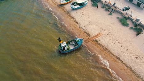 Aerial-view-of-fishing-boat-being-slowly-pulled-from-the-beach-to-the-sea