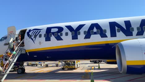 People-waiting-in-line-and-boarding-a-big-Ryanair-boeing-airplane-in-Malaga-international-airport-on-a-sunny-day-in-Spain,-holiday-vacation-time,-4K-shot