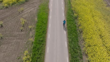 Drone-oblique-angle-follows-single-person-biking-along-path-at-midday-by-yellow-field