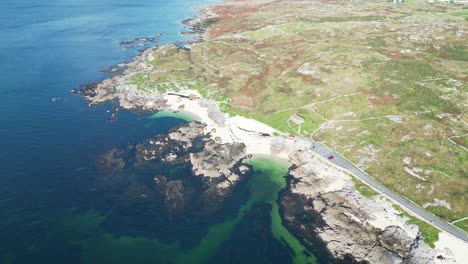 Aerial-view-of-a-rocky-coastal-landscape-with-clear-blue-water,-various-bays-and-beaches-and-a-coastal-road-at-coral-beach-in-connemara-galway,-ireland