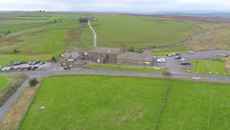 Sideways-and-pan-drone-footage-of-a-Yorkshire-country-pub-including-farmland,-fields-and-moorland,-country-roads-with-car-movement,-dry-stone-walls,-telegraph-poles