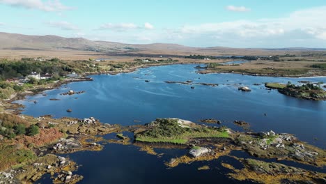 Aerial-dolly-backwards-shot-over-the-picturesque-connemara-lake-in-galway-in-ireland-with-views-of-the-reflective-blue-lake,-open-land-with-rolling-hills-and-vegetated-hills-on-a-sunny-day