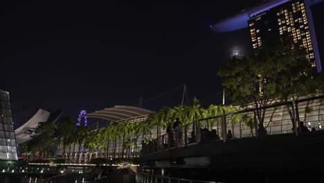 Blick-Nach-Oben-Entlang-Der-Beleuchteten-Promenade-Mit-Silhouetten-Von-Menschen-Neben-Geländern-In-Der-Marina-Bay,-Singapur