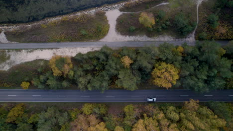 Top-down-view-of-a-vehicle-on-a-road-parallel-to-a-walking-path-and-autumn-trees