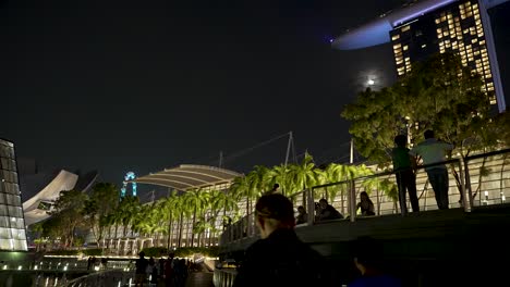 View-Along-Illuminated-Boardwalk-With-Silhouette-Of-People-Beside-Railings-At-Marina-Bay,-Singapore