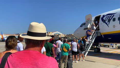 People-waiting-in-line-and-boarding-a-big-Ryanair-boeing-airplane-in-Malaga-international-airport-on-a-sunny-day-in-Spain,-summer-holiday-vacation-time,-4K-static-shot