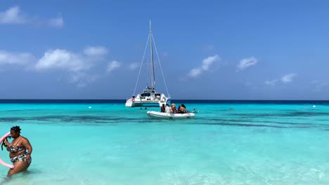 Crystal-clear-transparent-turquoise-water-in-tropical-Klein-Curaçao-beach,-people-swimming-from-charter-boat,-dream-vacation-destination-in-Little-Curaçao-the-Dutch-Caribbean-island,-4K-static-shot