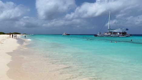 Crystal-clear-transparent-turquoise-water-in-tropical-Klein-Curaçao-white-sand-beach,-BlueFinn-charter-boat,-dream-vacation-destination-in-Little-Curaçao-the-Dutch-Caribbean-island,-4K-static-shot