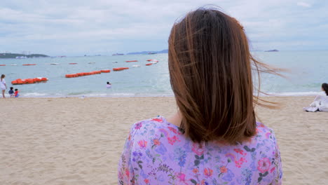 Eine-Frau-Blickt-Auf-Die-Anderen-Strandbesucher,-Die-Am-Strand-Von-Pattaya-In-Der-Provinz-Chonburi-In-Thailand-Schwimmen-Und-Sitzen
