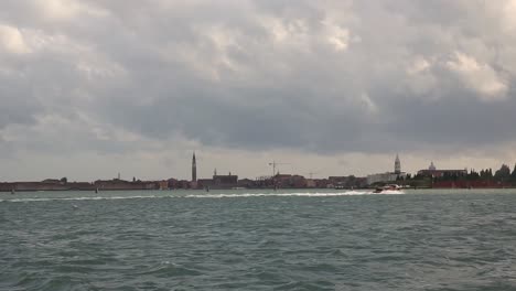 Speed-boat-drive-on-cloudy-day-in-front-of-Venice-old-town-panorama,-Italy