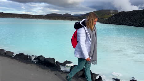Beautiful-blonde-girl-walking-by-turquoise-water-of-blue-lagoon-in-Iceland