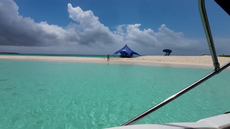 Beach-seen-from-inside-boat-float-on-caribbean-sea,-woman-walking-on-white-sand-background
