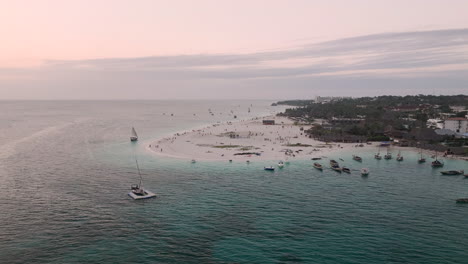 Panorama-of-coastline-at-sunset,-drone-view-of-sandy-beach,-turquoise-ocean,palm-tree,-luxury-resort-and-people,-Zanzibar,Tanzania