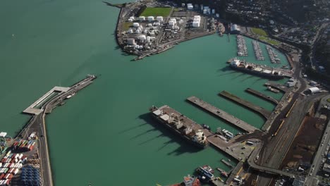 Lyttleton,-New-Zealand-harbour-with-ships-and-cranes,-container-yard,-aerial-reveal-to-horizon