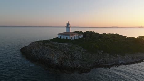 Aerial-ascend-to-reveal-Alcanada-lighthouse-on-rocky-island,-vibrant-white-facade-and-orange-roof