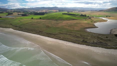 Katiki-Beach-and-scenic-farmland-of-New-Zealand,-mountains-on-horizon