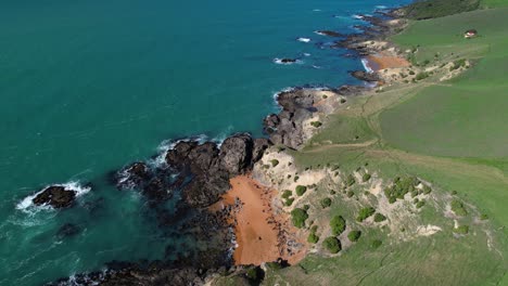 Small-red-sand-beach-surrounded-by-dark-cliffs,-New-Zealand-East-Coast,-Katiki-Point