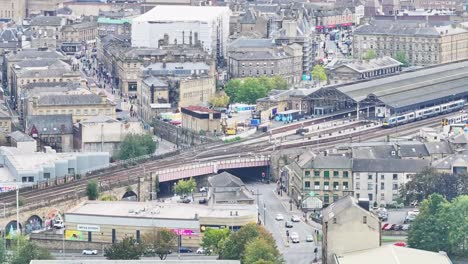 Bustling-train-transit-station-in-Huddersfield-as-cars-drive-below,-aerial-overview