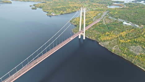 Aerial-View-Of-Vehicles-Crossing-Hogakustenbron-Bridge-Over-Tranquil-Sea-And-Autumn-Forest-In-Sweden
