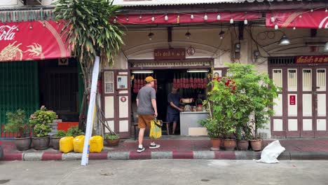 Point-of-view-of-a-shopkeeper-preparing-dried-food,-Chinese-Sausages,-and-a-tourist-walking-over-and-checking-it-out-in-Yaowarat-Chinatown,-Bangkok,-Thailand