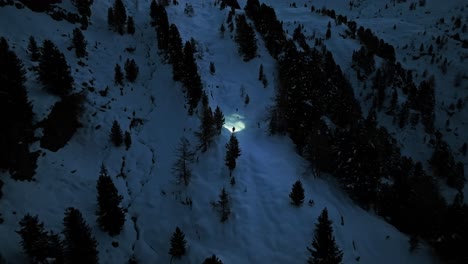Aerial-view-of-a-lone-hiker,-illuminated-by-a-headlamp,-trekking-through-a-snowy-mountain-landscape-at-night