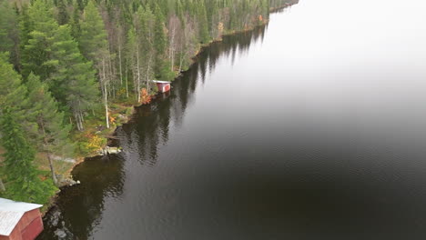 Suecia---El-Lago-Espejo-En-Otoño-Muestra-Un-Bosque-Colorido-En-Un-Día-Nublado,-Complementado-Con-Casas-De-Pescadores-Rojas-A-Lo-Largo-De-La-Orilla-Del-Agua---Drones-Volando-Hacia-Adelante