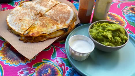 Delicious-pulled-chicken-quasadilla-with-guacamole,-hot-sauces-and-sour-cream-at-a-Mexican-restaurant,-spicy-slow-cooked-chicken-tortilla-with-cheese,-4K-shot
