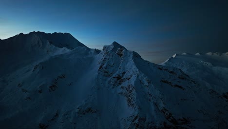 Aerial-view-of-the-South-Tyrolean-mountains-during-the-blue-hour-of-a-winter-morning,-with-the-sun’s-first-light-illuminating-the-peaks