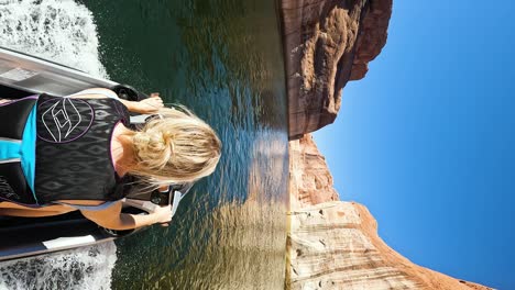 Blonde-hair-woman-drive-jet-ski-on-Lake-Powell-canyon,-POV-vertical-shot