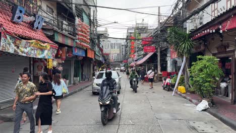 Street-scene-of-tourists-sauntering-and-vehicles-moving-slowly-in-Yaowarat-Chinatown,-Bangkok,-Thailand