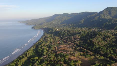 Costa-Rica-drone-flying-over-the-green-dense-forest-and-mountains-on-a-sunny-day-with-the-pacific-sea-on-the-side