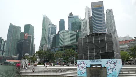 Merlion-Fountain-Statue-Covered-With-Scaffolding-Due-To-Repair-Works-At-Merlion-Park-In-Marina-Bay,-Singapore-With-Office-Skyscrapers-In-Background