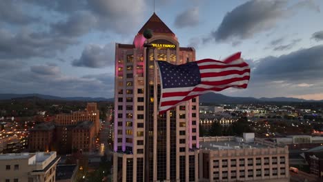 Bandera-Americana-Ondeando-En-El-Centro-De-Roanoke,-Virginia,-Con-El-Rascacielos-De-Wells-Fargo-En-Segundo-Plano.