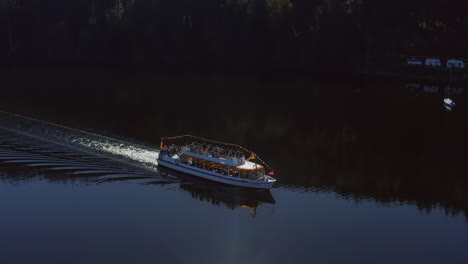 Tracking-shot-of-a-tourist-boat-on-a-lake-in-the-Black-Forest-passing-by-a-campsite-at-summer