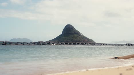 slow-motion-shot-of-Chinamans-Hat-Mokoli'i-in-Oahu-Hawaii-with-small-waves-crashing-on-the-beach-in-the-foreground
